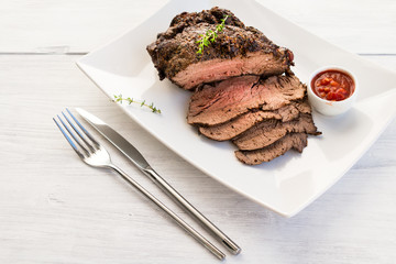 Roast beef on white plate with red sauce and thyme twig.