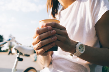 Woman in a white T-shirt is holding a paper cup of coffee outdoors in summer