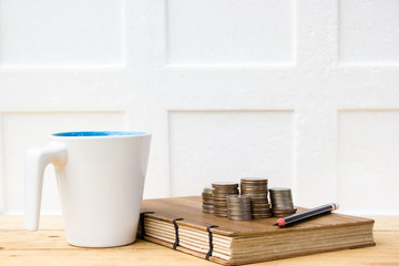 Coins, notebook and white cup on wooden table on white background. Conceptual business and relaxing in nature.