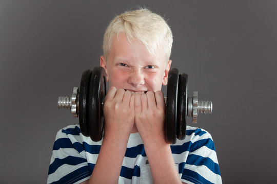 Blond male child trying to lift heavy dumbbell