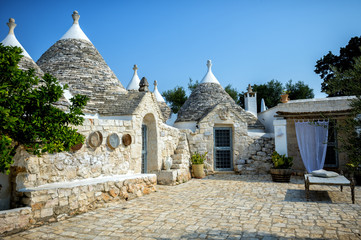 Typical trulli buildings with conical roofs, among green plants and flowers, main touristic district, Val d' Itria, Apulia region, Southern Italy, - obrazy, fototapety, plakaty