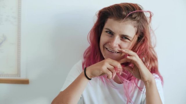 Young attractive hipster millennial girl with pink rebel hair plays with it and makes mustache out of it. Cute pretty female is fooling around, careless and funny, smiles and laughs