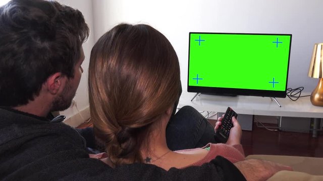 Couple Changing Channel On TV Green Screen, Zoom In. Couple watching television green screen relaxed at home. Zooming behind models shoulders