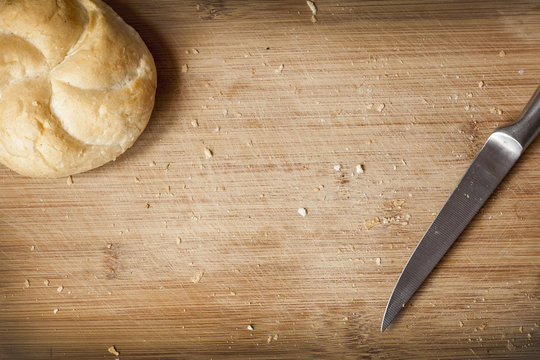 Kaiser roll and kitchen knife on cutting board with crumbs