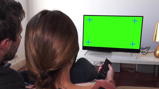 Couple Changing TV Channels Over Green Screen, Panning Shot. Couple watching television green screen relaxed at home. Pan camera behind models shoulders