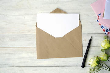 Top view of envelope and blank greeting card with rose flowers on white wooden background.