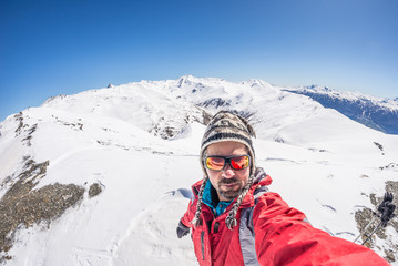 Fototapeta na wymiar Adult alpin skier with beard, sunglasses and hat, taking selfie on snowy slope in the beautiful italian Alps with clear blue sky. Concept of wanderlust and adventures on the mountain.