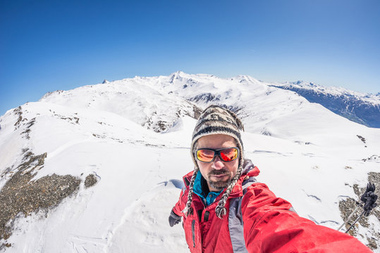 Adult alpin skier with beard, sunglasses and hat, taking selfie on snowy slope in the beautiful italian Alps with clear blue sky. Concept of wanderlust and adventures on the mountain.