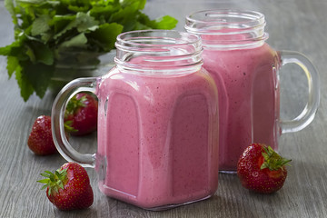 Strawberry smoothies in a glass bottle, mint leaves and whole strawberry berries on a gray wooden background.