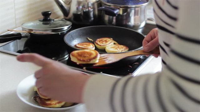 Cook pancakes on a frying pan/A woman cookes pancakes in the kitchen on a frying pan