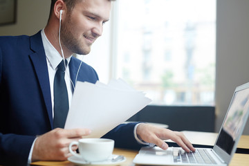 Fototapeta na wymiar Modern businessman typing on laptop and listening to music in earphones