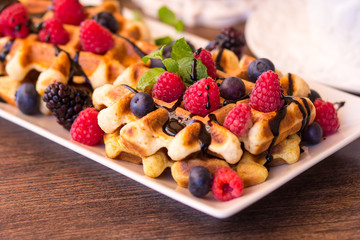 Belgium waffles with raspberries, chocolate and syrup on a plate.