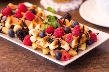 Belgium waffles with raspberries, chocolate and syrup on a plate.
