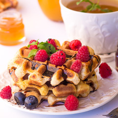 Belgium waffles with raspberries, chocolate and syrup on a plate.