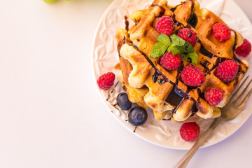 Belgium waffles with raspberries, chocolate and syrup on a plate.