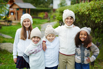 Happy children of various ages standing close together and looking at camera smiling, dressed in matching white knit clothes posing as siblings or family