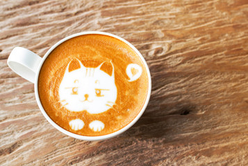 Cute cat face of latte art coffee in white cup on old wooden table with copy space , warm light