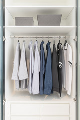 clothes hanging on rail in wooden white wardrobe