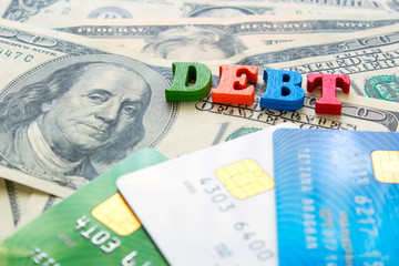 Fototapeta premium Word DEBT on a pile of money of dollar bills and bank credit cards