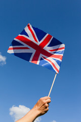 British flag in hand against blue sky.