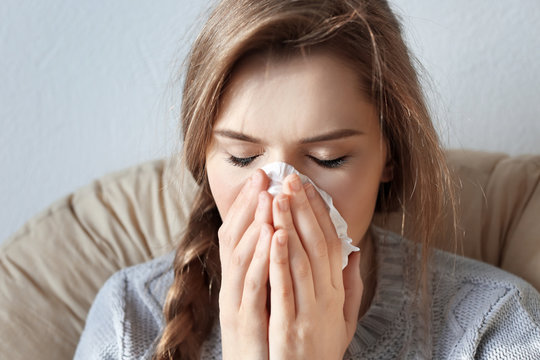 Young ill woman with tissue sitting on lounge at home