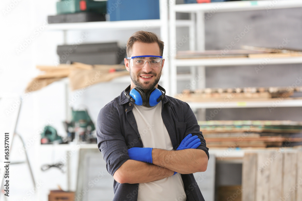 Wall mural Young smiling carpenter standing with crossed hands in workshop