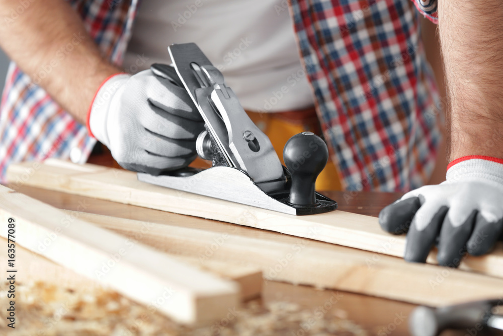 Wall mural Carpenter planing wooden plank on table, closeup