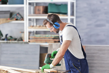 Carpenter sawing timber in light workshop