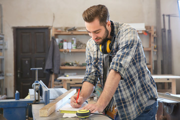 Carpenter applying marking onto drawing in workshop