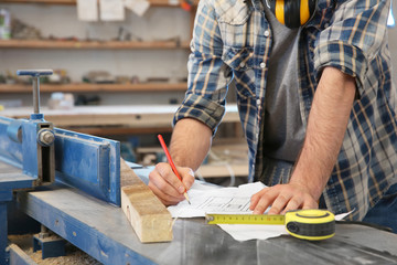 Carpenter applying marking onto drawing in workshop, closeup