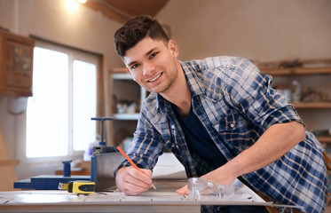Handsome young carpenter checking drawing at table in workshop