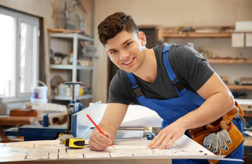 Handsome young carpenter checking drawing at table in workshop