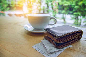 Soft tone of Money and credit card in a leather wallet with blur of hot coffee on wooden table and bill slip with natural background