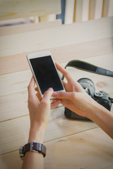 Woman using smartphone with blank screen and camera on the wood table.