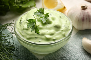Delicious yogurt sauce with parsley leaves in bowl on kitchen table