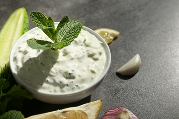 Delicious yogurt sauce in bowl with ingredients on dark background