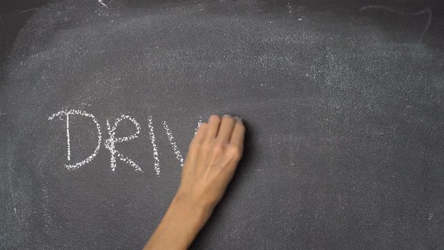 Woman's hand writing "DRIVE SAFE" with white chalk on blackboard