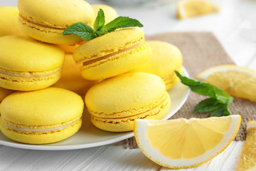 Plate with tasty lemon macarons on white wooden table, closeup