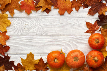 Autumn leaves and pumpkins over old wooden background