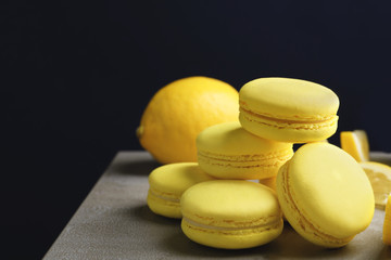 Tasty lemon macarons on table against dark background, closeup