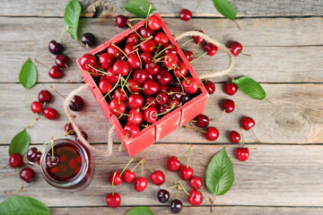 Sweet cherries in red crate with juice in glass jar on grey wooden table