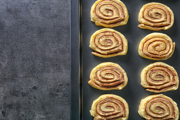 Raw cinnamon rolls on baking tray on kitchen table