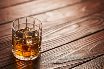 Glass of whiskey with ice cubes on wooden table