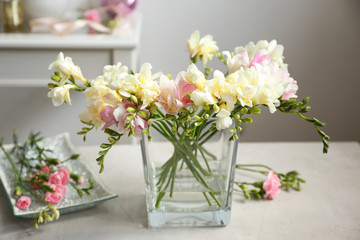Beautiful bouquet with freesia flowers in glass vase on blurred background