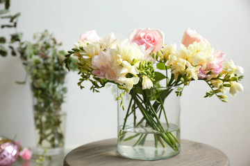 Beautiful bouquet with freesia flowers in glass vase on light background
