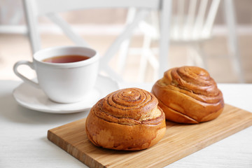 Wooden board with yummy cinnamon rolls and cup of tea on white table