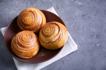 Fototapeta premium Brown round plate with yummy cinnamon rolls on kitchen table