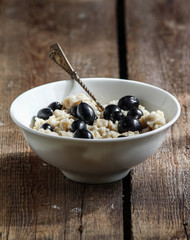 Oatmeal with blackcurrant berries in a white plate on a wooden surface