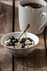 Oatmeal with blackcurrant berries in a white plate on a wooden surface
