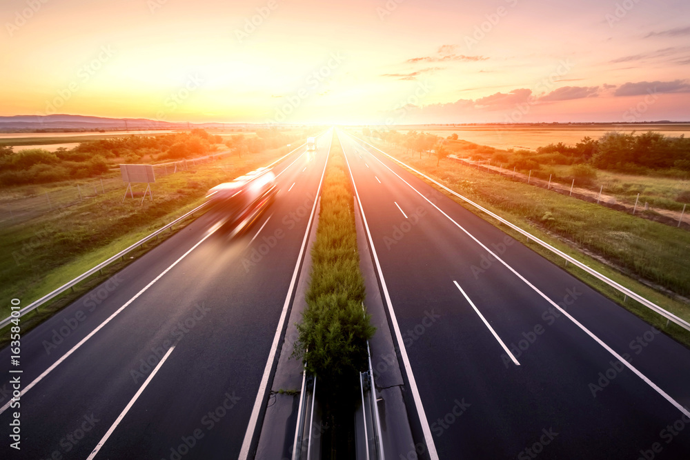 Wall mural highway landscape in a strong back light at sunset with motion blurred truck